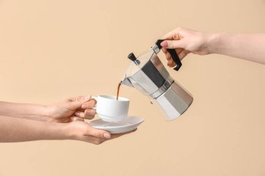 Kadın gayzer kahve makinesinden bej arka planda fincana espresso döküyor.