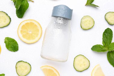 Beyaz arka planda salatalık limonatası hazırlamak için malzemelerle dolu bir spor şişesi.