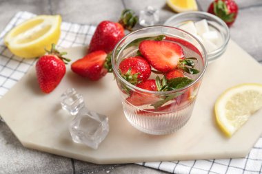 Çilekli limonata ve gri fayans zemininde bir bardak içki hazırlamak için malzemelerle dolu bir pano.