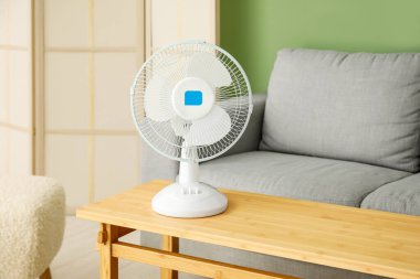 Oturma odasının içinde modern elektrikli vantilatör olan ahşap masa.