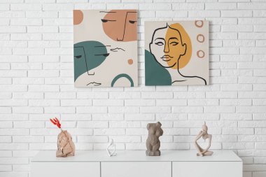 Beyaz tuğla duvarın yanında farklı resimler olan şık bir dolap.