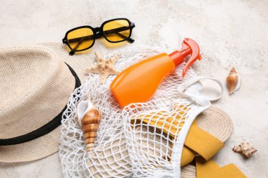 Güneş gözlüklü string çantası, bir şişe güneş kremi ve hafif grunge arka planda plaj aksesuarları.