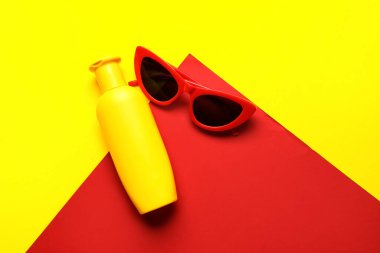 Arka planda güneş kremi şişesi olan güneş gözlüğü.