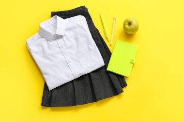 Sarı arka planda taze elma ve kırtasiye malzemesi olan şık okul üniforması.