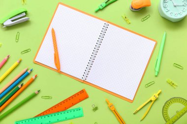 Boş defter ve yeşil arkaplanda farklı kırtasiye malzemeleri