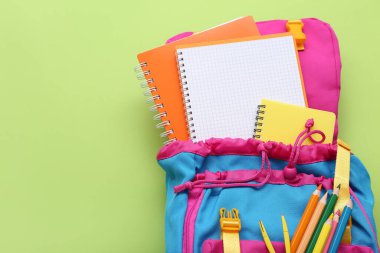 Yeşil zemin üzerinde boş defter ve kırtasiye malzemesi olan sırt çantası