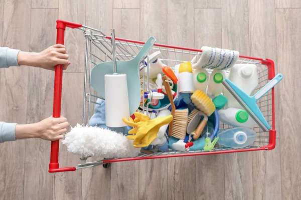 stock image Woman with shopping cart full of cleaning supplies on wooden floor, top view