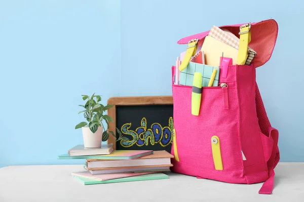 粉红校服背包 装有笔记本 小黑板和家居用品 放在靠近蓝色墙壁的白桌面上 — 图库照片