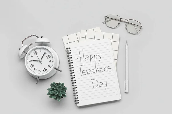 Notebooks with text HAPPY TEACHERS DAY, eyeglasses and alarm clock on grey background