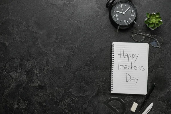 Notebook with text HAPPY TEACHERS DAY, alarm clock and eyeglasses on grunge black background