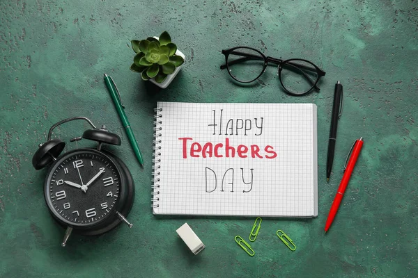 Notebook with text HAPPY TEACHERS DAY, alarm clock and different stationery on grunge green background