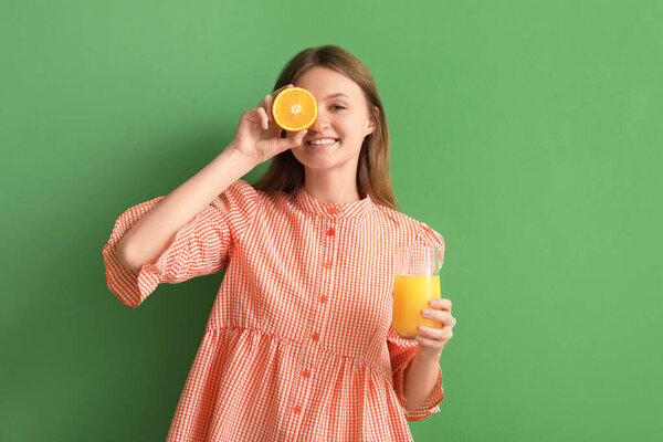 Teenage girl with orange and glass of juice on green background