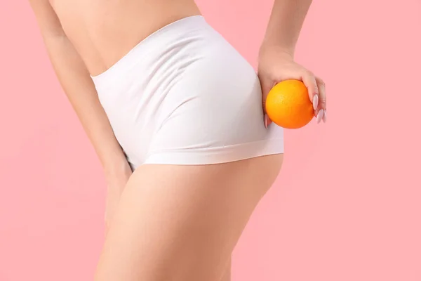Young woman with cellulite problem and orange on pink background, closeup