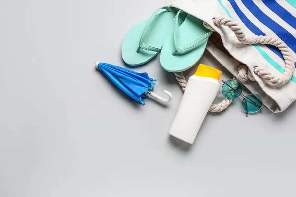stock image Bag with sunglasses, flip flops, mini umbrella and bottle of sunscreen cream on grey background