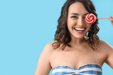 Mavi arka planda lolipopu olan genç bir kadın, yakın plan.