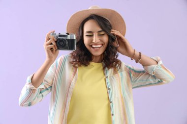 Leylak arka planında fotoğraf makinesi olan yaz şapkalı genç bir kadın.