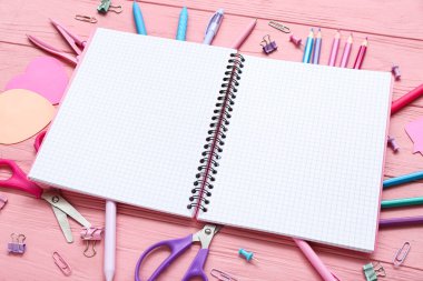 Boş defter ve pembe ahşap arka planda farklı kırtasiye malzemeleri