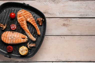 Hafif ahşap arka planda ızgara somon bifteği ve sebzeli kızartma tavası.