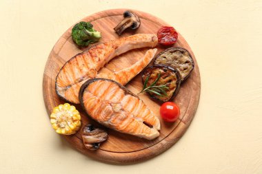 Sarı arka planda ızgara somon bifteği ve sebzeli ahşap tahta tahta.