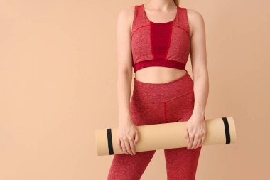 Spor giyimli genç bir kadın ve bej arka planda yoga minderi var.