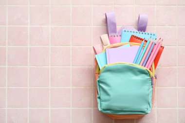 Pembe karo arka planda not defterleri, kalemler ve işaretlerle dolu renkli okul çantası.