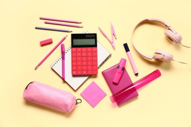 Kulaklıklı modern hesap makinesi ve soluk sarı arka planda farklı kırtasiye malzemesi.