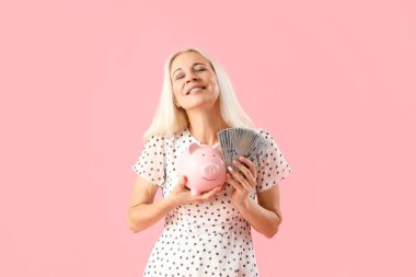 Dolar banknotları ve pembe arka planda kumbarası olan olgun bir kadın.