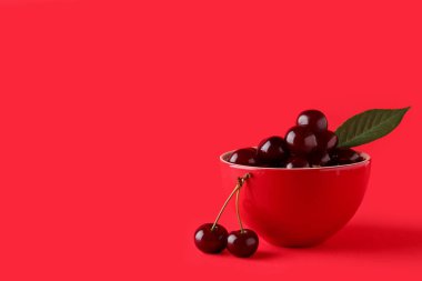 Tatlı kirazlı kase ve kırmızı arka planda yaprak