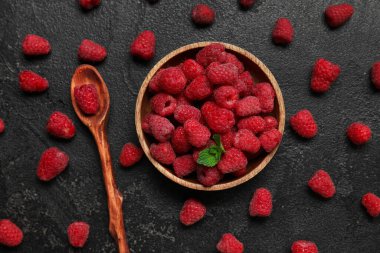 Koyu arkaplanda taze ahududu ve kaşık olan ahşap kase.