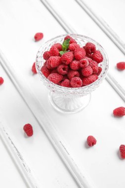 Hafif ahşap zemin üzerinde taze ahududu olan cam kase.