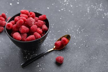 Koyu arkaplanda taze ahududu ve kaşık olan kase, yakın plan.