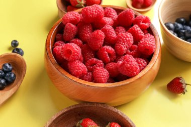 Sarı arka planda taze ahududu, yaban mersini ve çilek kaseleri