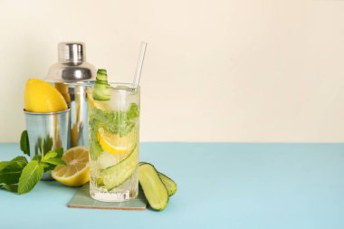 Barmen aletleriyle beyaz duvarın yanındaki mavi masada bir bardak mojito.
