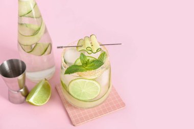 Bir bardak salatalık mojito ve pembe arka planda jigger.