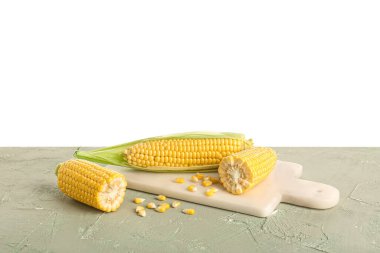 Beyaz arka planda gri masada taze mısır koçanı ve tohumları olan tahta