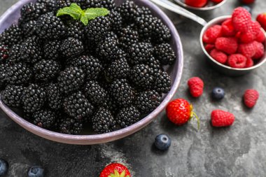 Gri arka planda taze böğürtlenli kase, yakın plan.