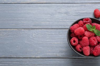 Gri ahşap arka planda taze ahududu ve naneli kase, yakın plan.