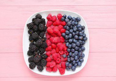 Pembe ahşap arka planda taze ahududu, yabanmersini ve böğürtlen tabağı.