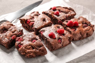 Gri masadaki ahududulu çikolatalı browni parçalarının olduğu bir kağıt.