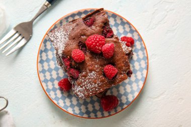 Açık mavi masada ahududulu çikolatalı browni tabağı.