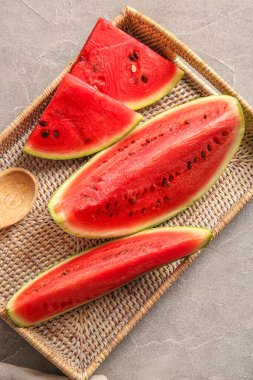 Gri masada taze karpuz parçaları olan hasır tepsi.