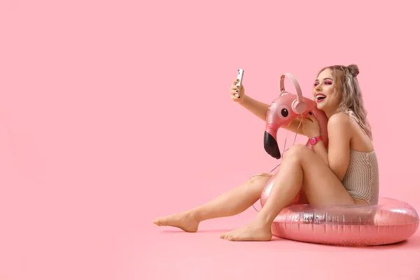 stock image Young woman in swimsuit with mobile phone and inflatable ring on pink background