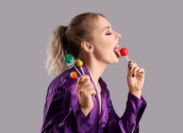 若い女性食べるロリポップ上の灰色の背景 — ストック写真