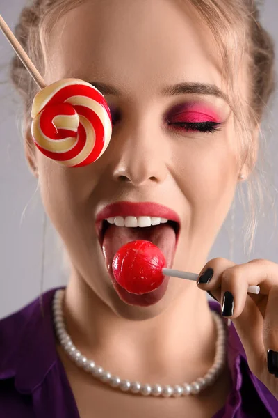 若い女性食べるロリポップ上の灰色の背景 — ストック写真