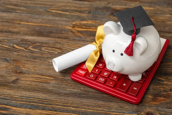 茶色の木製の背景に卒業証書と電卓付き卒業キャップの貯金箱 学生ローンの概念 — ストック写真