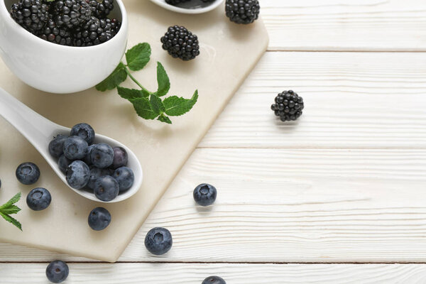 Bowl with fresh blackberry and blueberry on light wooden background, closeup
