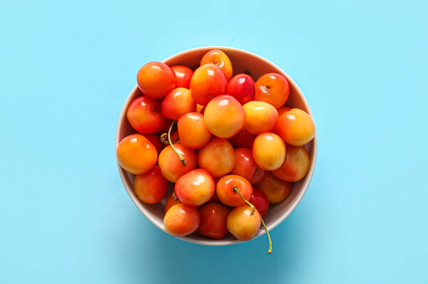 Bowl with sweet yellow cherries on blue background