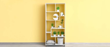 Sarı duvarın yanında evleri olan beyaz raf ünitesi.