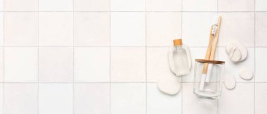 Bambu diş fırçaları, bir şişe serum ve hafif fayans zemininde spa taşları ve metin için yeri olan tutucu.