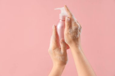 Pembe arka planda sıvı sabun olan eller